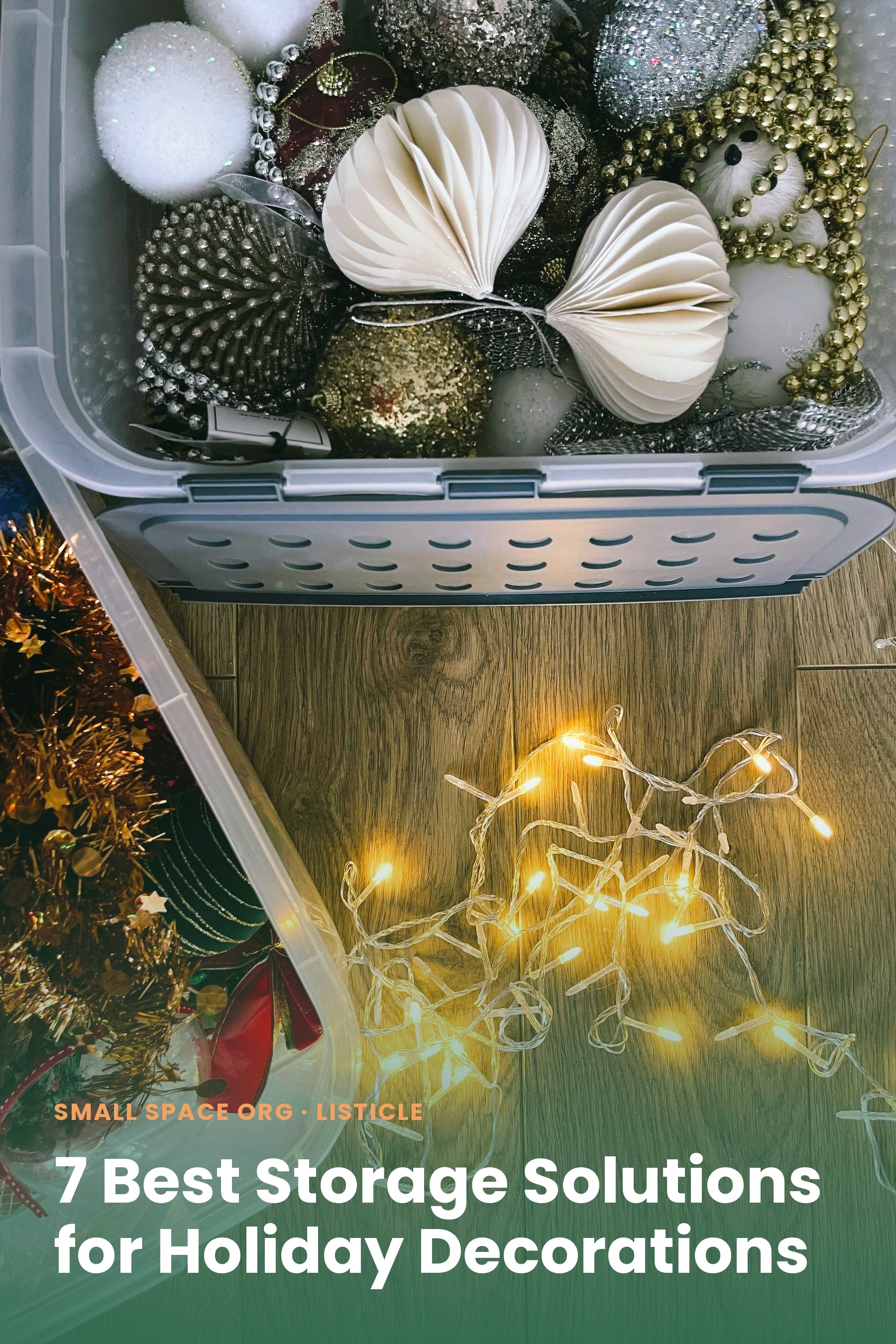 A clear plastic bin full of ornaments and garland beside a loose strand of warm string lights on a wood floor
