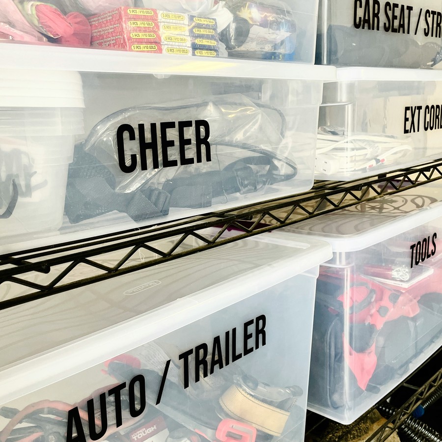 Labeled clear plastic storage bins stacked on a shelf