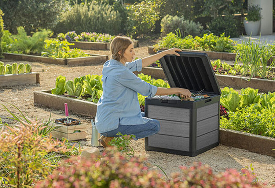 Graphite gray Keter Cortina 30 gallon resin deck box on a garden patio, lid open