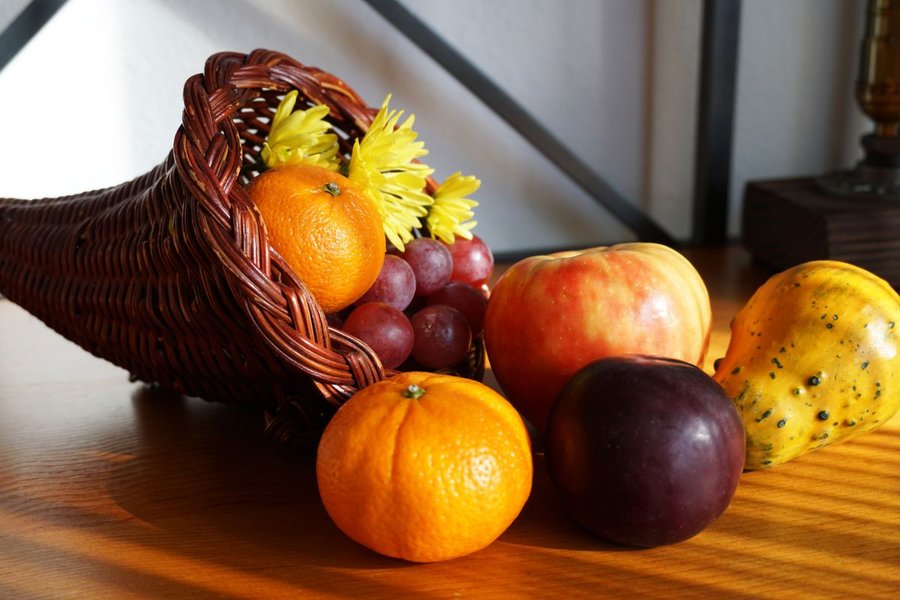 A woven rattan cornucopia basket filled with fruit and gourds