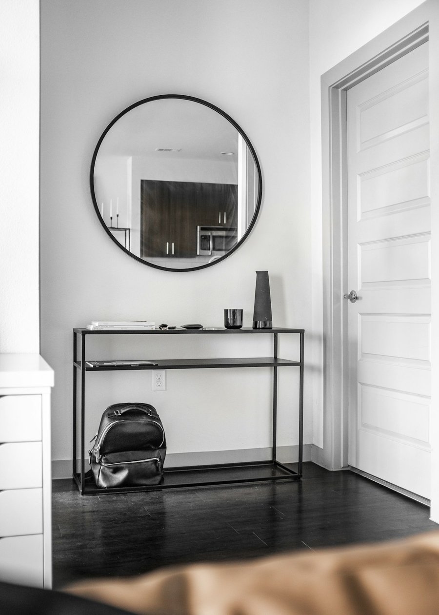 Round mirror with a slim black metal frame mounted above an entryway console table