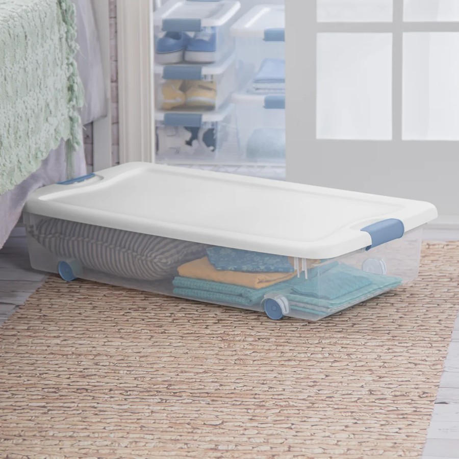 Clear wheeled plastic storage box with white latching lid tucked under a bed
