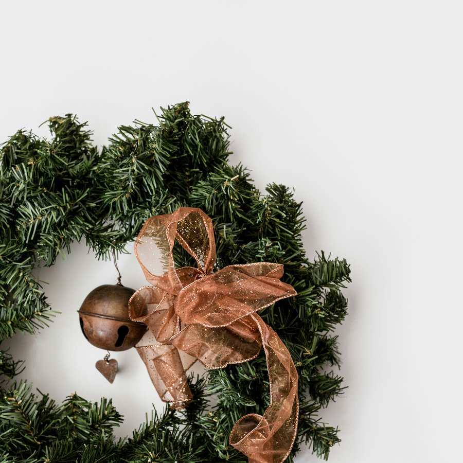 A green pine wreath with a copper bow and bell on a white background, a stock photo that stands in for wreath storage